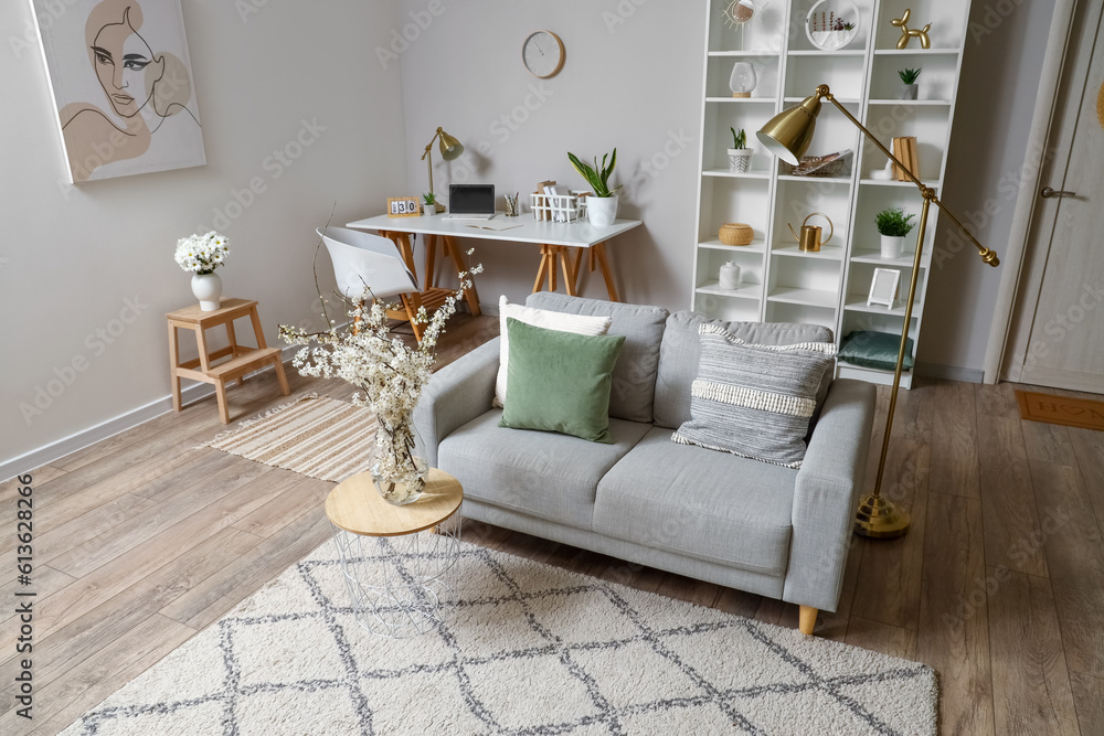 Interior of living room with grey sofa and blossoming tree branches on coffee table