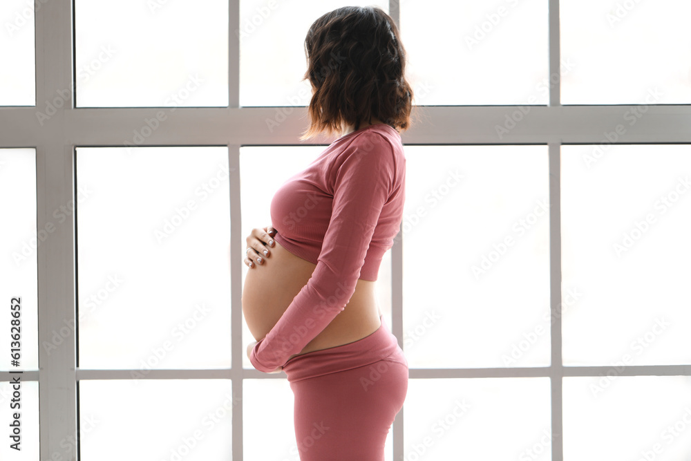 Sporty pregnant woman near window at home