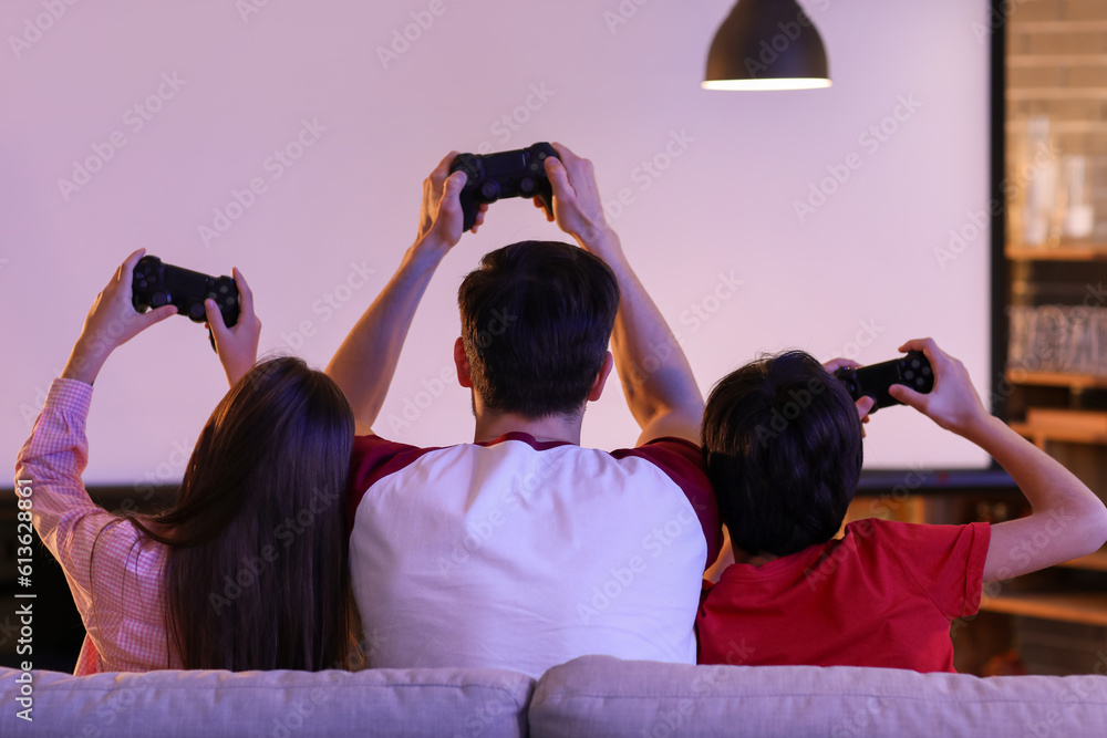 Father with his little children playing video game at home in evening, back view