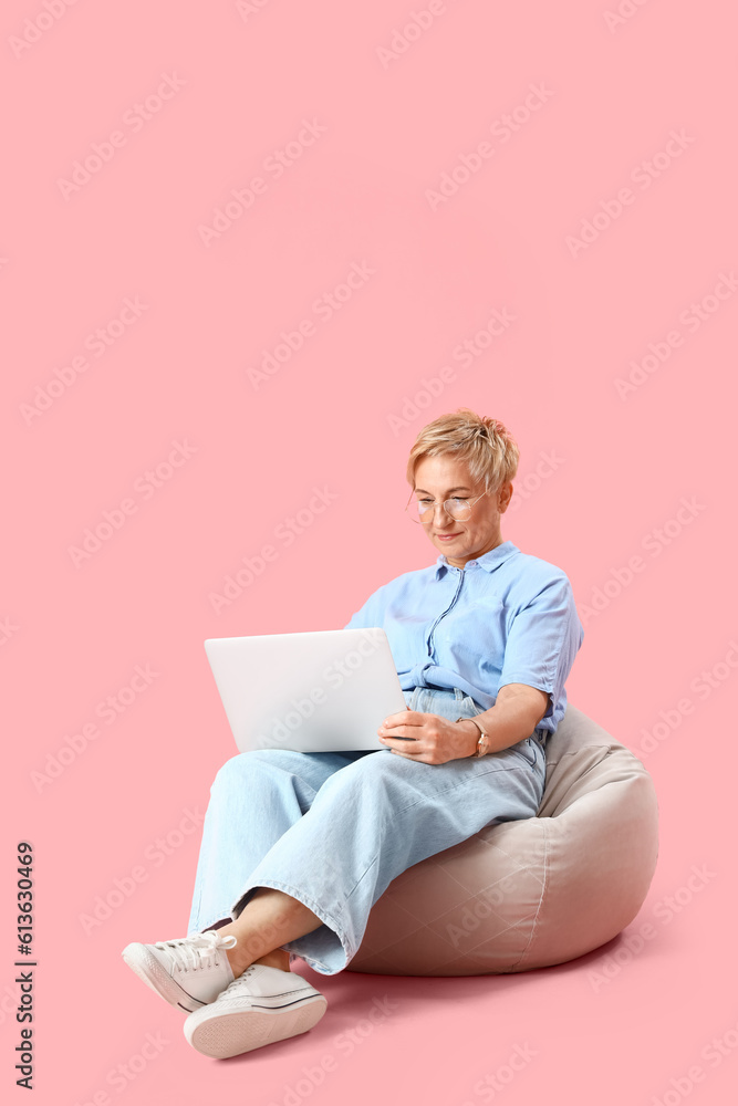 Mature female programmer working with laptop on pink background