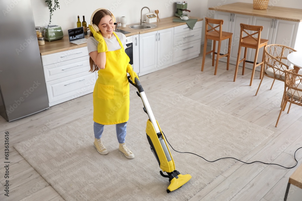 Young woman with headphones hoovering carpet in kitchen