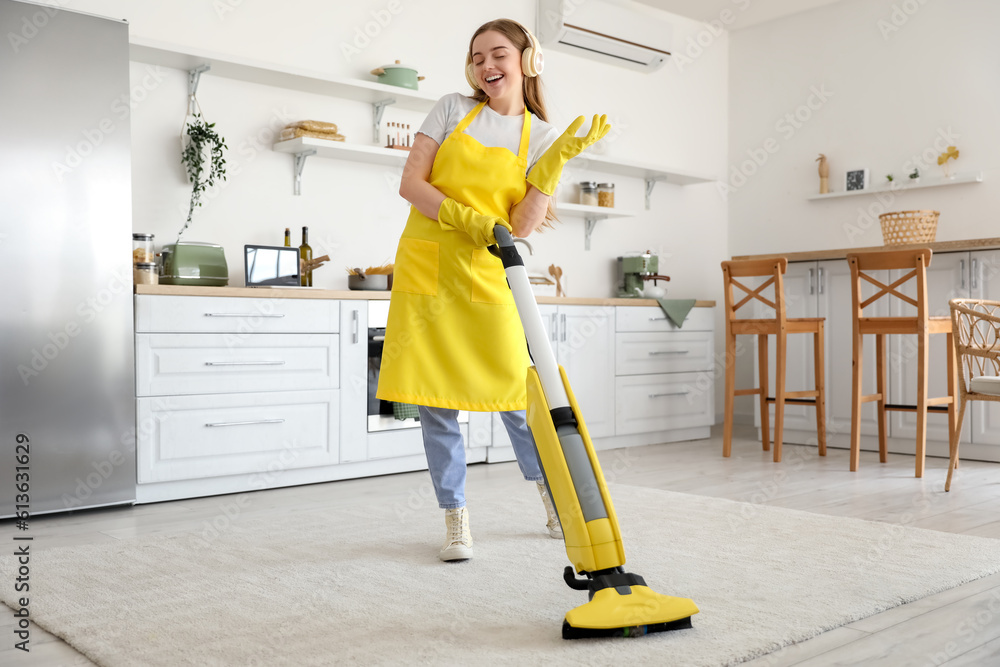 Young woman with headphones hoovering carpet in kitchen