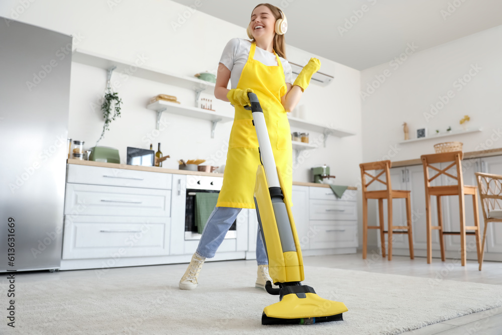 Young woman with headphones hoovering carpet in kitchen