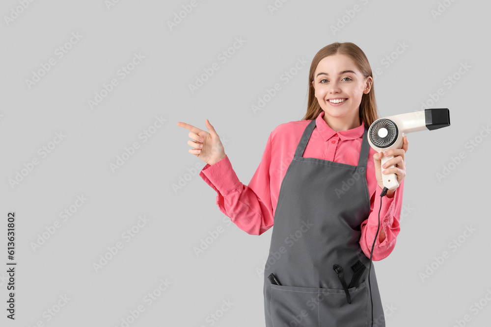 Female hairdresser with dryer pointing at something on grey background