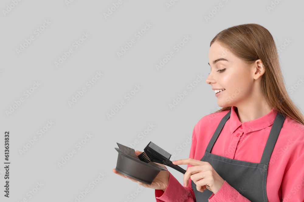 Female hairdresser with bowl and brush for hair dye on grey background, closeup