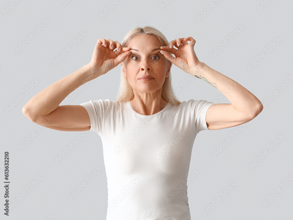 Mature woman doing face building exercise on light background