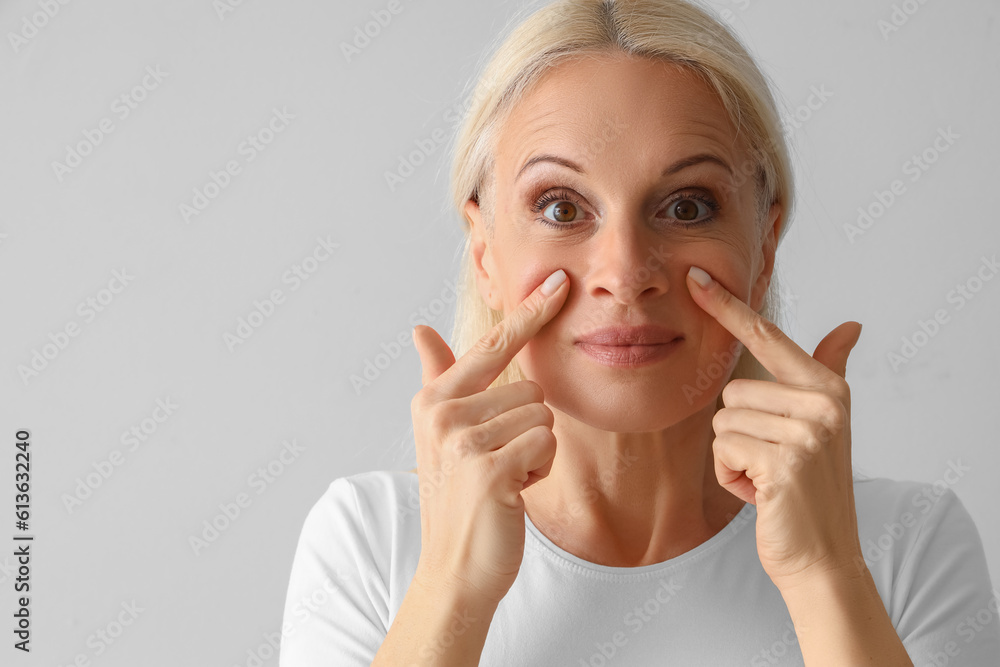 Mature woman doing face building exercise on light background, closeup