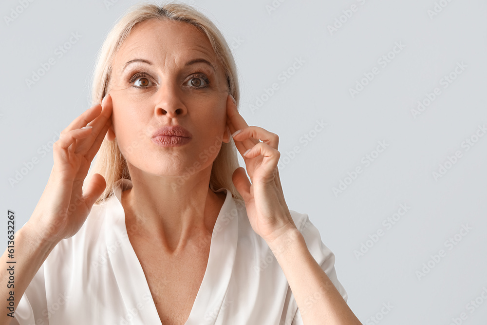 Mature woman doing face building exercise on light background, closeup