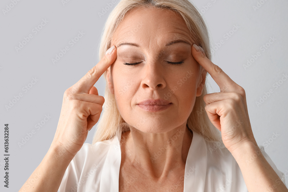 Mature woman doing face building exercise on light background, closeup