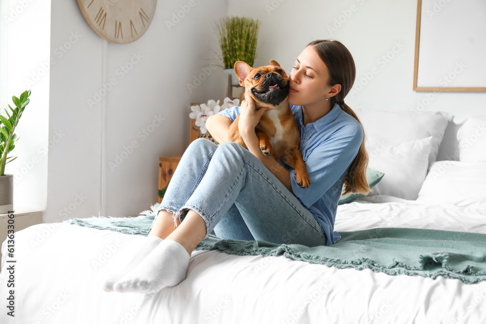 Young woman with cute French bulldog in bedroom