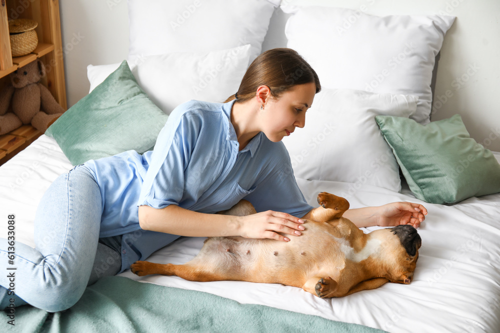 Young woman with cute French bulldog lying in bedroom