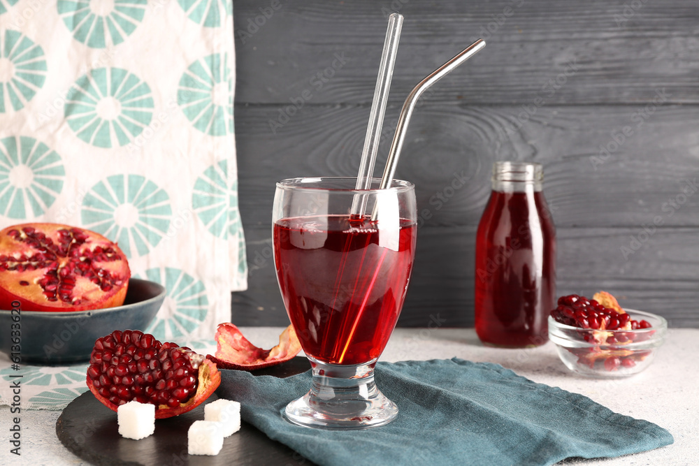 Bowl with fresh pomegranate and glass of juice on table near grey wooden wall