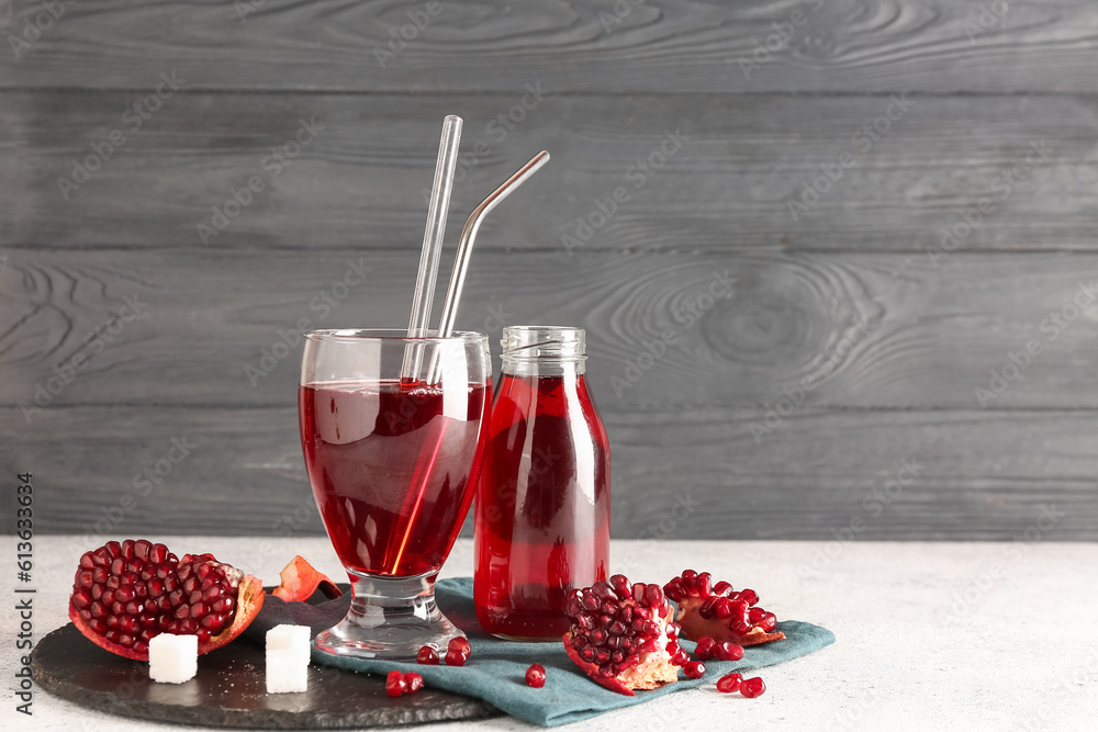 Bottle and glass of fresh pomegranate juice on table near grey wooden wall