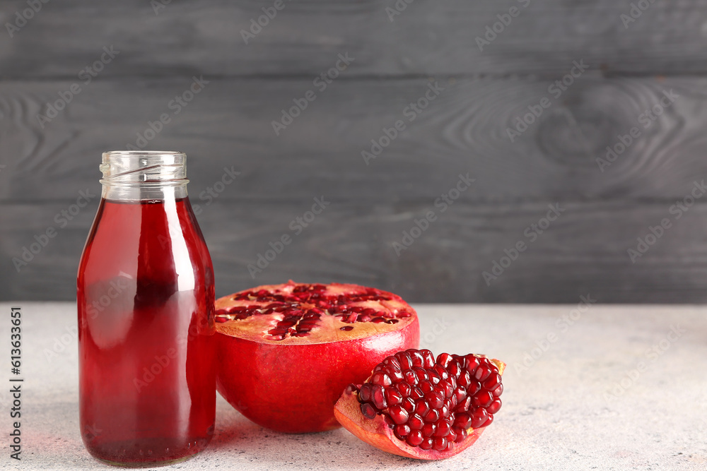 Bottle of fresh pomegranate juice on table near grey wooden wall