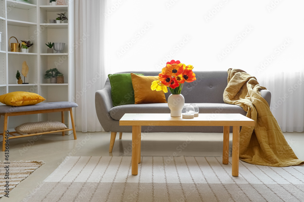 Interior of light living room with cozy grey sofa and tulip flowers on coffee table