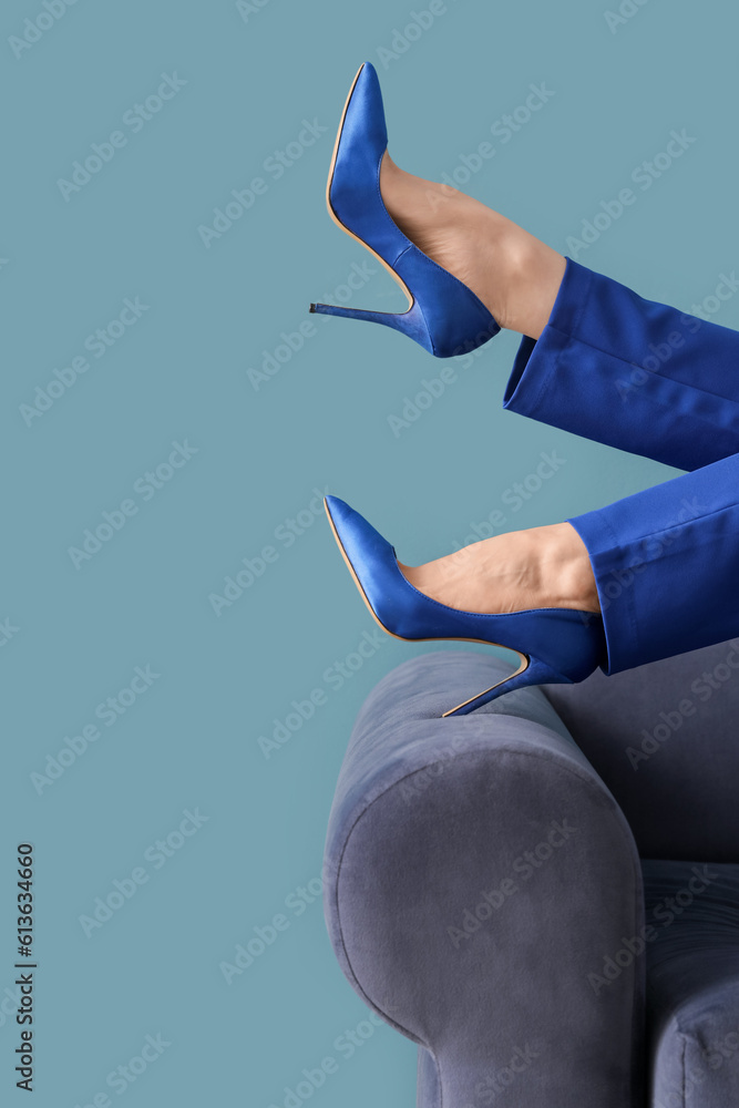 Female legs in high heels on sofa against blue background