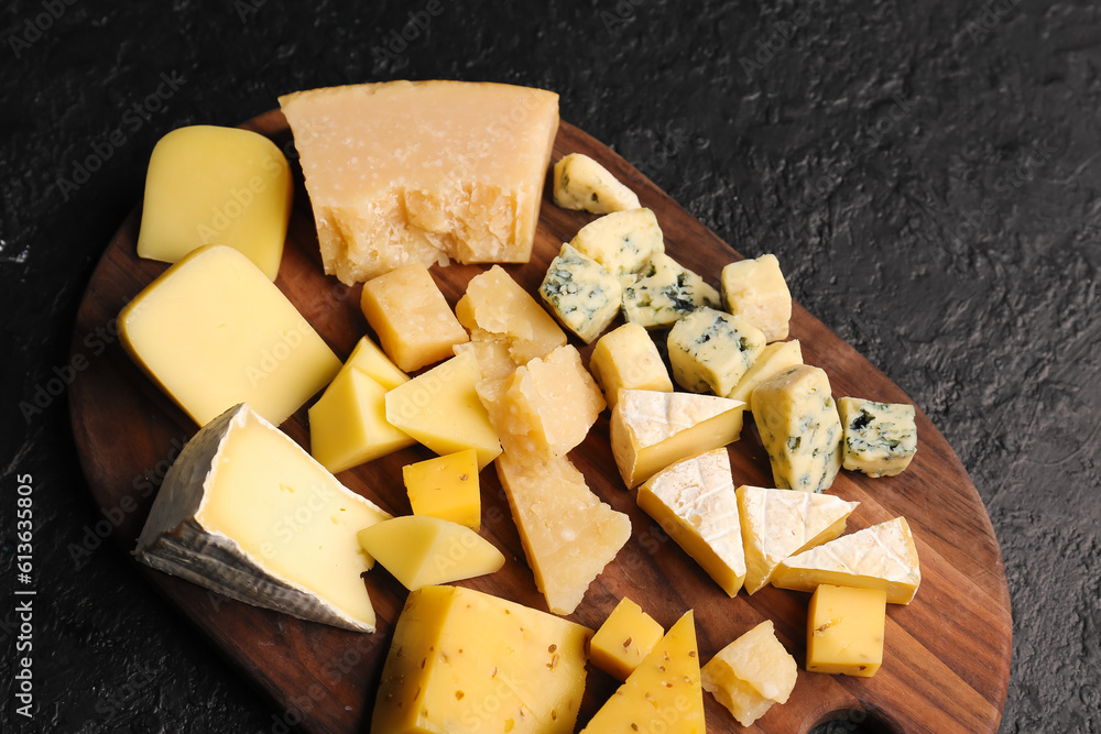 Wooden board with pieces of tasty cheese on dark background