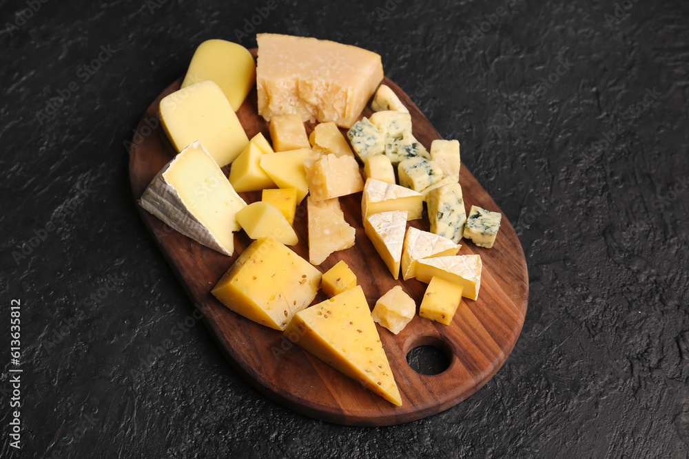 Wooden board with pieces of tasty cheese on dark background