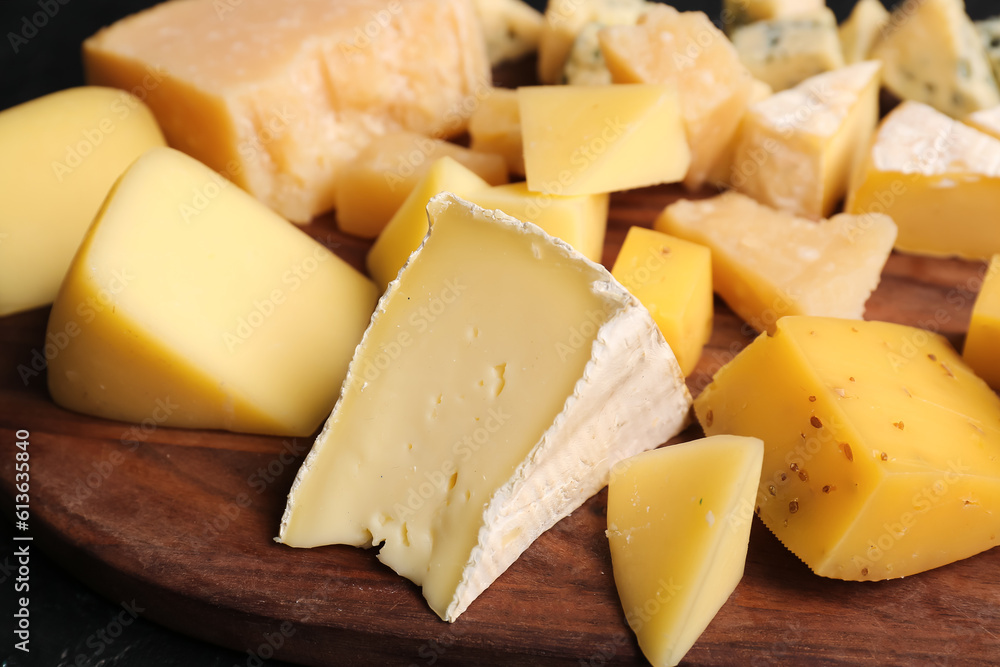 Wooden board with pieces of tasty cheese on table, closeup