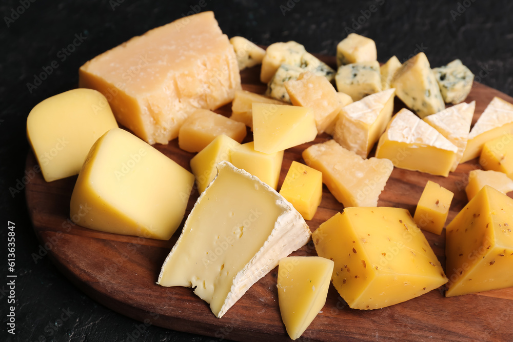 Wooden board with pieces of tasty cheese on table, closeup