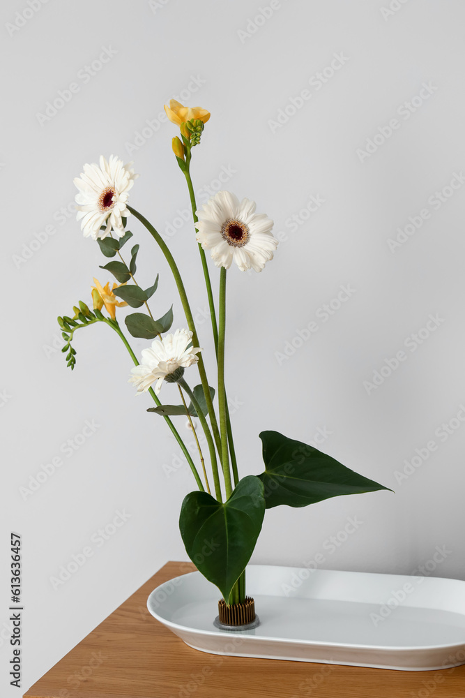 Beautiful ikebana on table near light wall