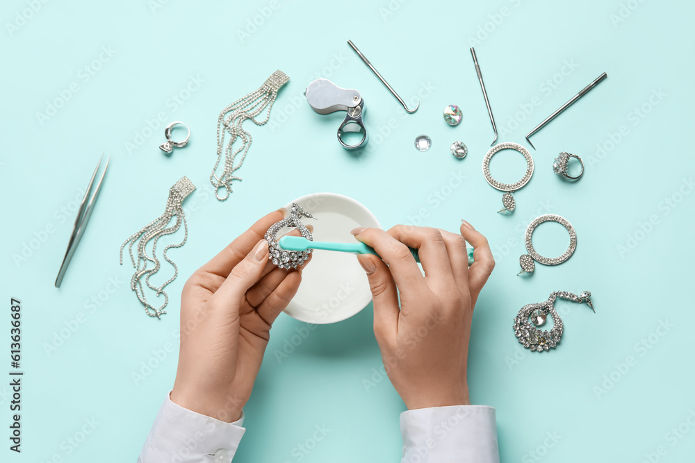 Woman cleaning beautiful earring with toothbrush on color background