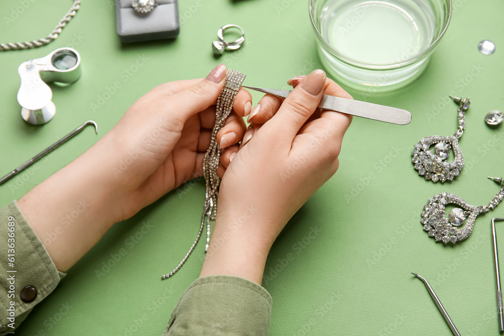 Woman cleaning beautiful jewelry on green background, closeup