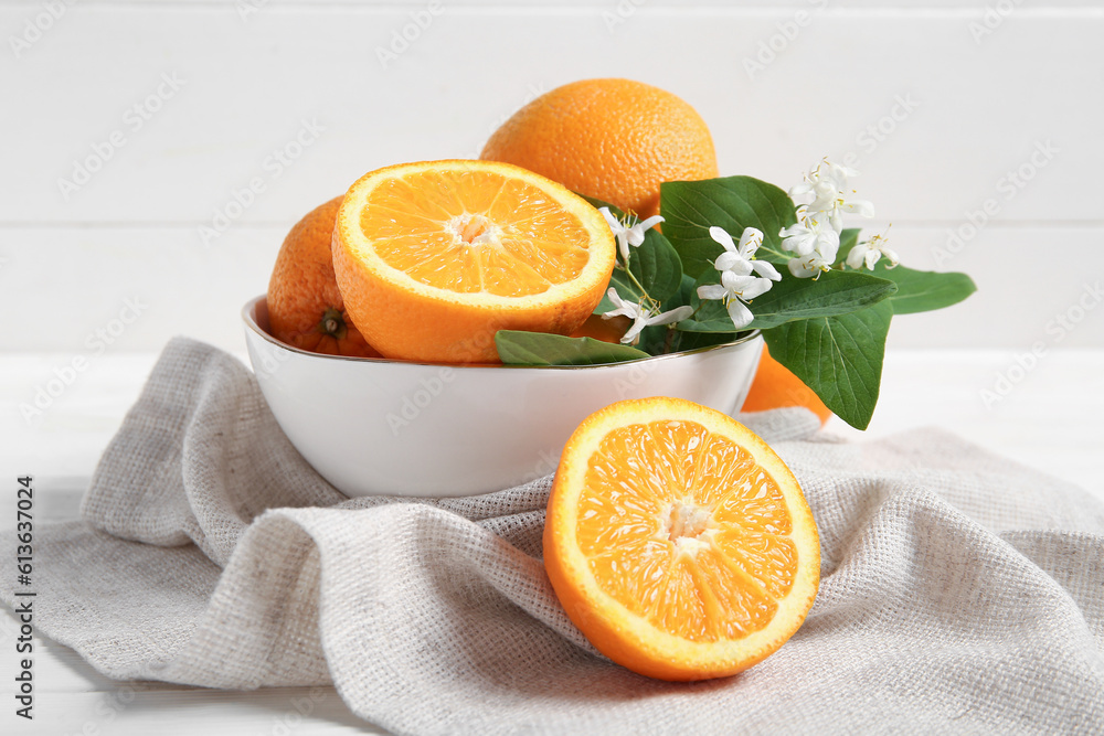 Bowl of oranges with blooming branch on white table