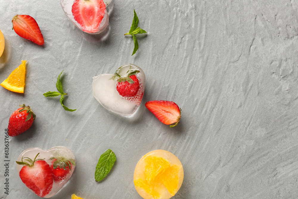 Fresh strawberry and pieces of orange frozen in ice on grey background