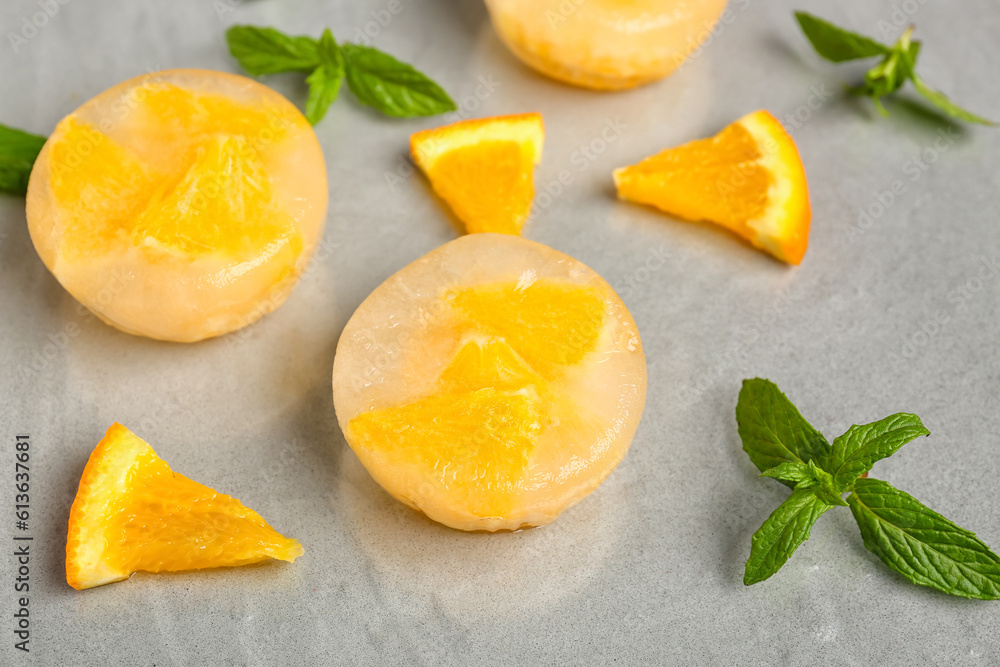 Pieces of orange frozen in ice on grey background