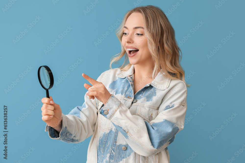 Young woman pointing at magnifier on blue background