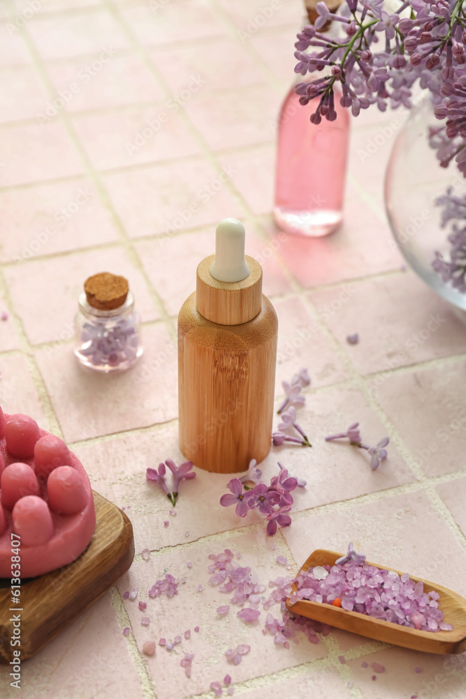 Bottles of cosmetic oil with beautiful lilac flowers and sea salt on pink tile table