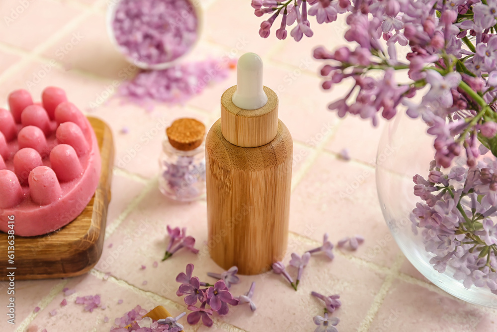 Bottles of cosmetic oil with beautiful lilac flowers and sea salt on pink tile table