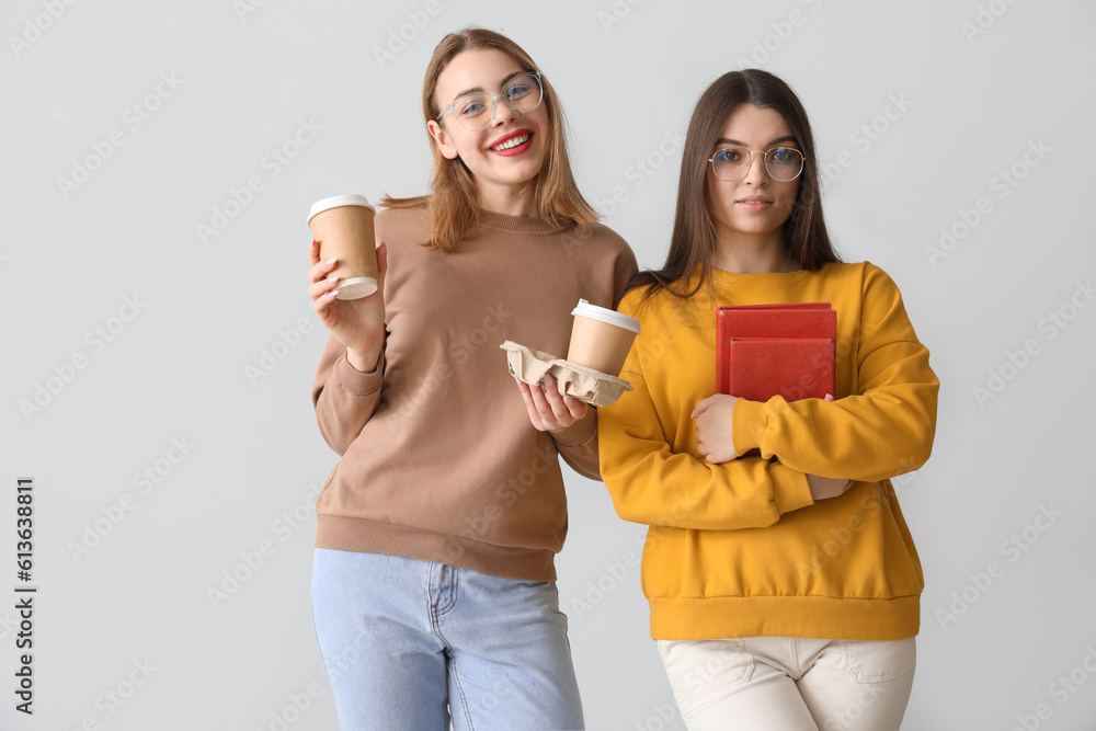 Female friends with cups of coffee and books on light background