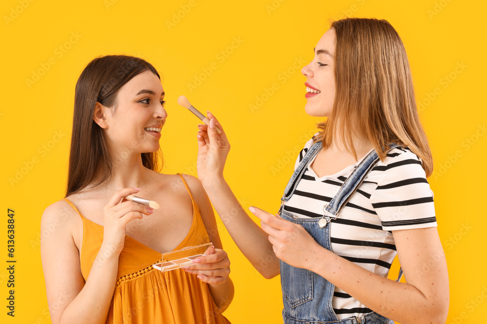 Female friends doing makeup on yellow background