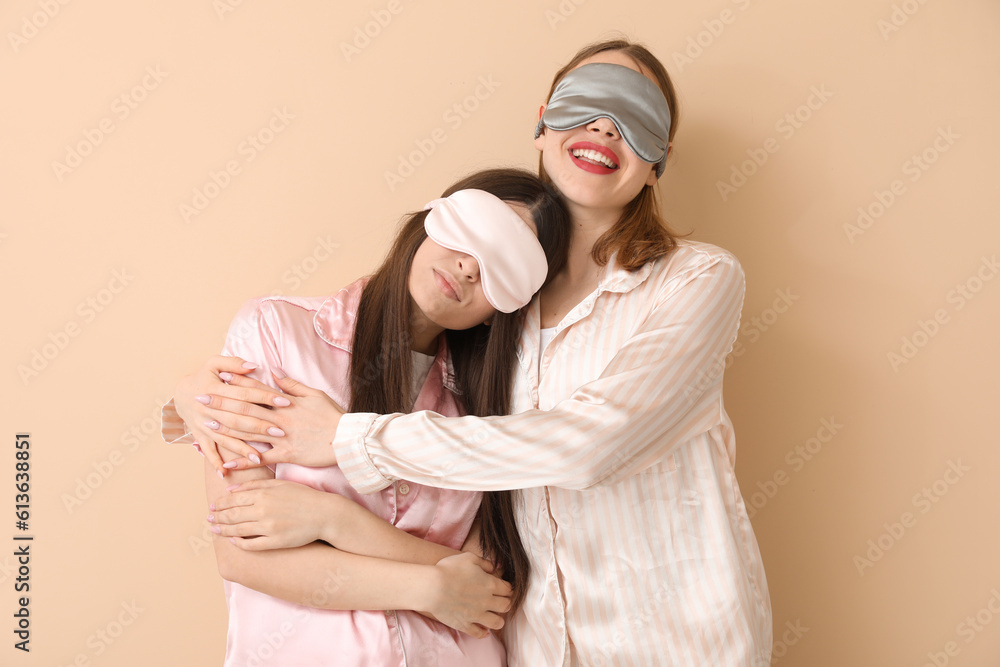 Female friends in sleeping masks hugging on beige background