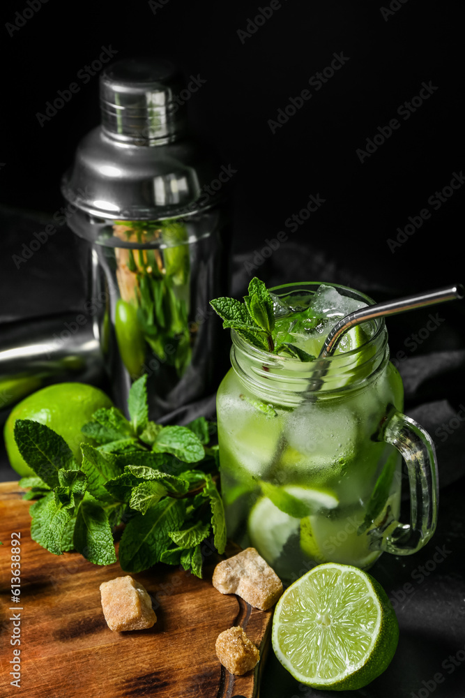 Mason jar of cold mojito and ingredients on dark background