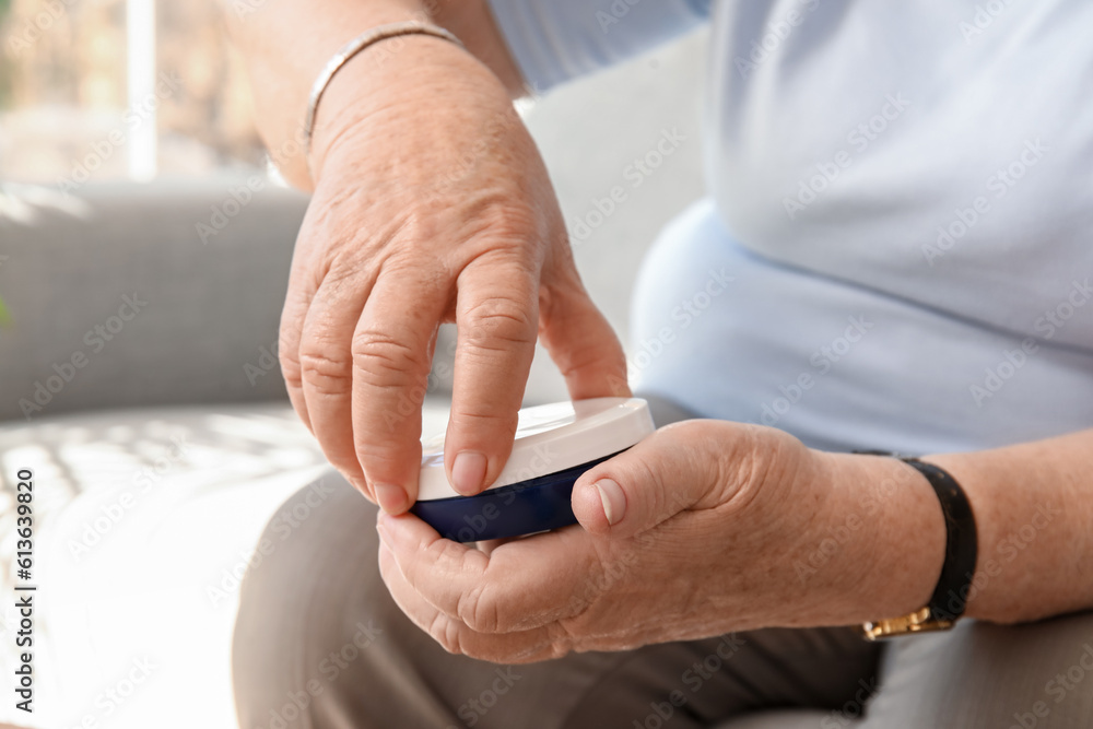 Senior woman with jar of cream at home, closeup