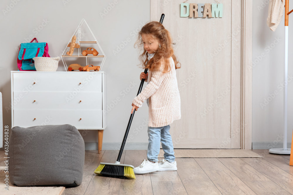 Cute little girl sweeping floor with broom at home