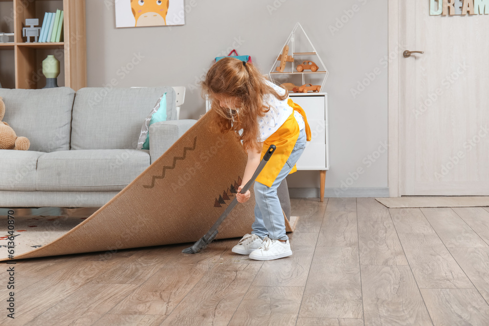 Cute little girl sweeping floor under carpet with broom at home