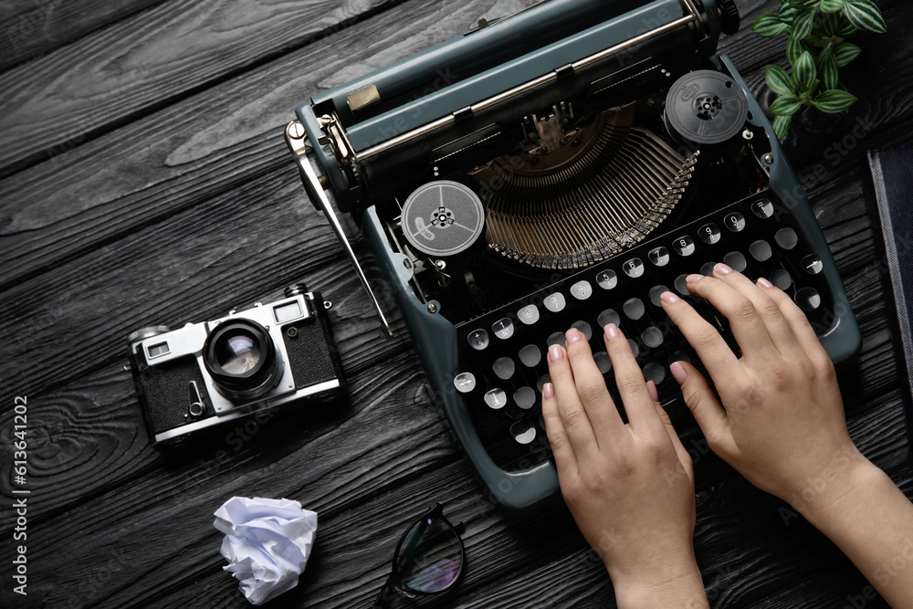 Woman typing on typewriter with camera, eyeglasses and crumpled paper on black wooden background