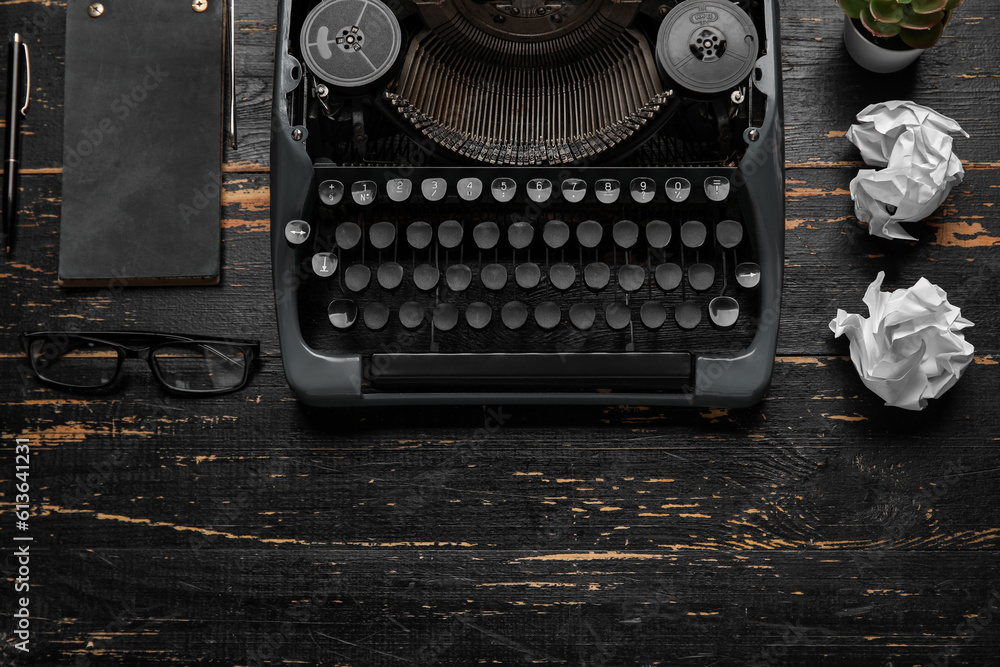 Vintage typewriter with notebook, eyeglasses and crumpled paper on dark wooden background