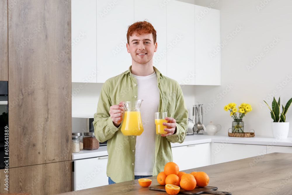 Young man with glass and jug of orange juice in kitchen