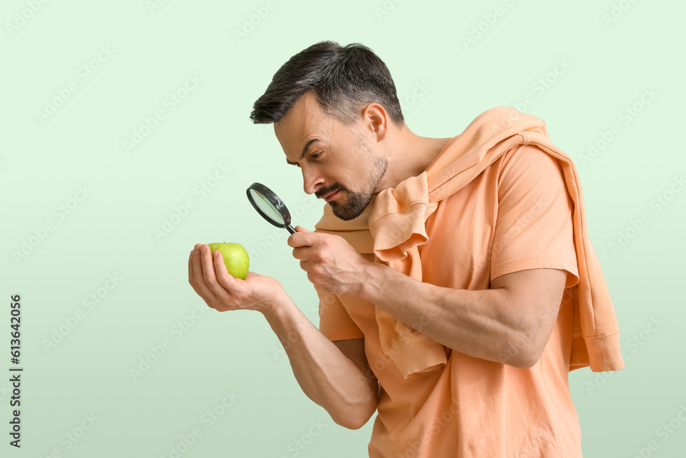 Handsome man with magnifier and apple on green background