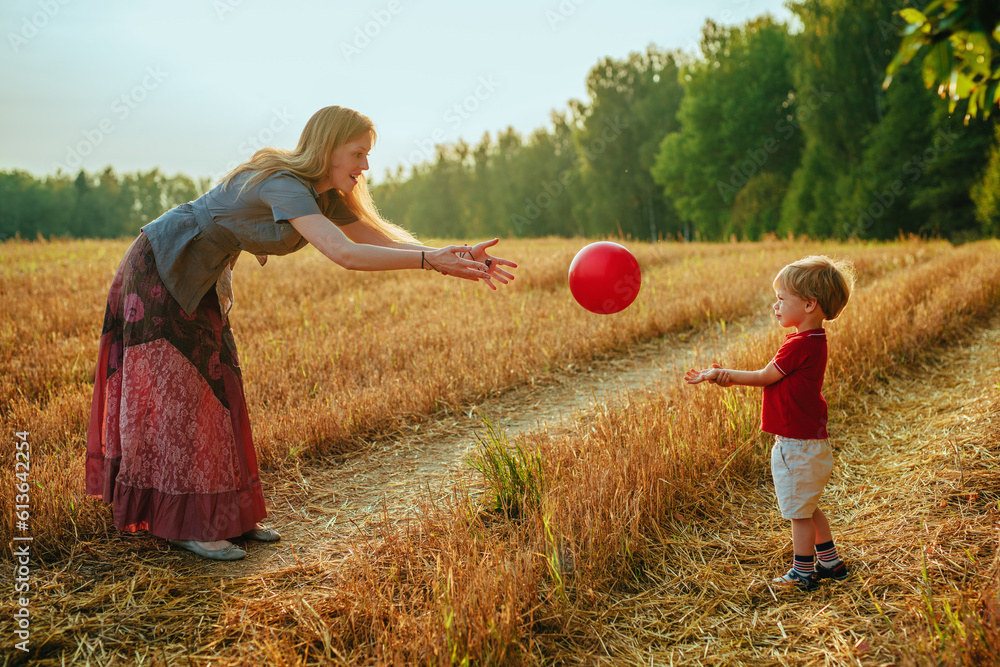 Young mother plays ball with her two-year-old son in a field