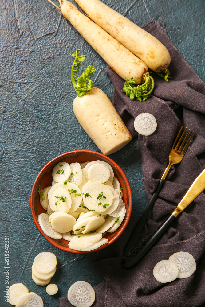 Bowl with slices of fresh daikon radish on dark background