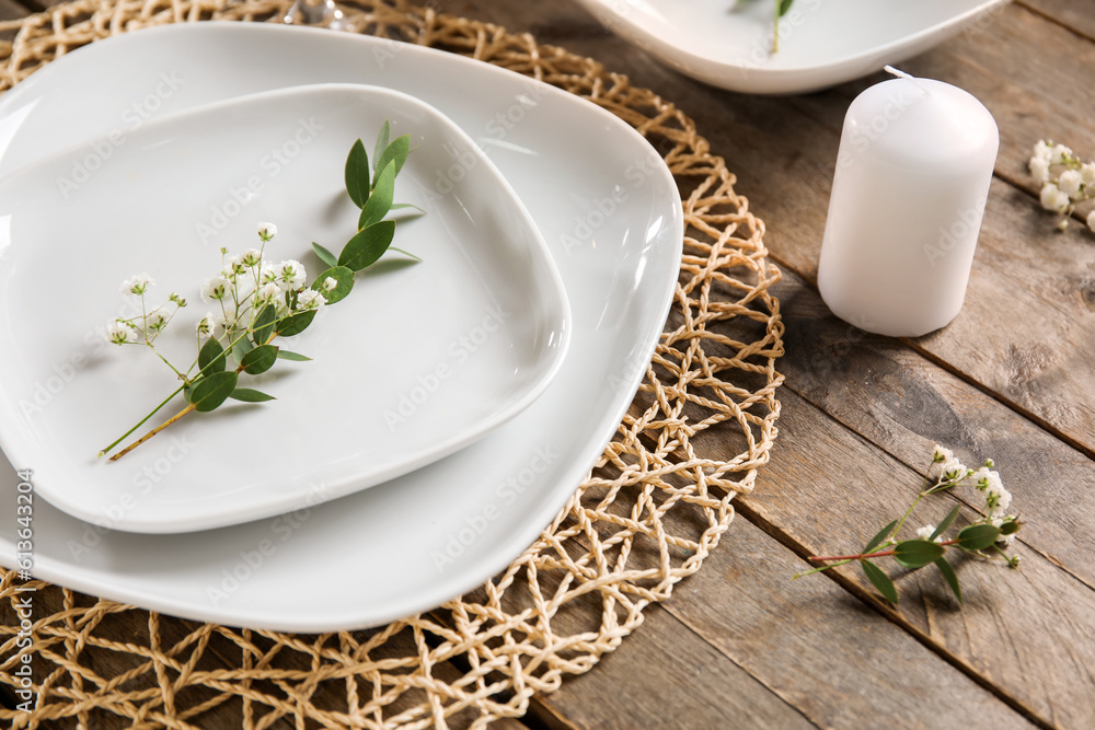 Wicker mat with stylish table setting and candle on brown wooden background