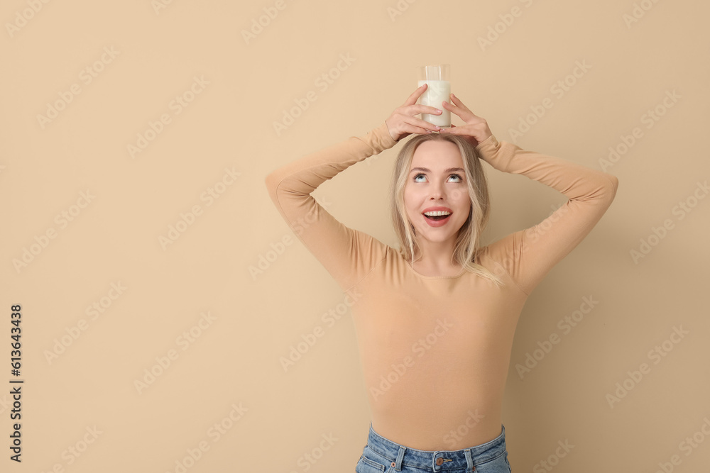 Young woman with glass of milk on beige background