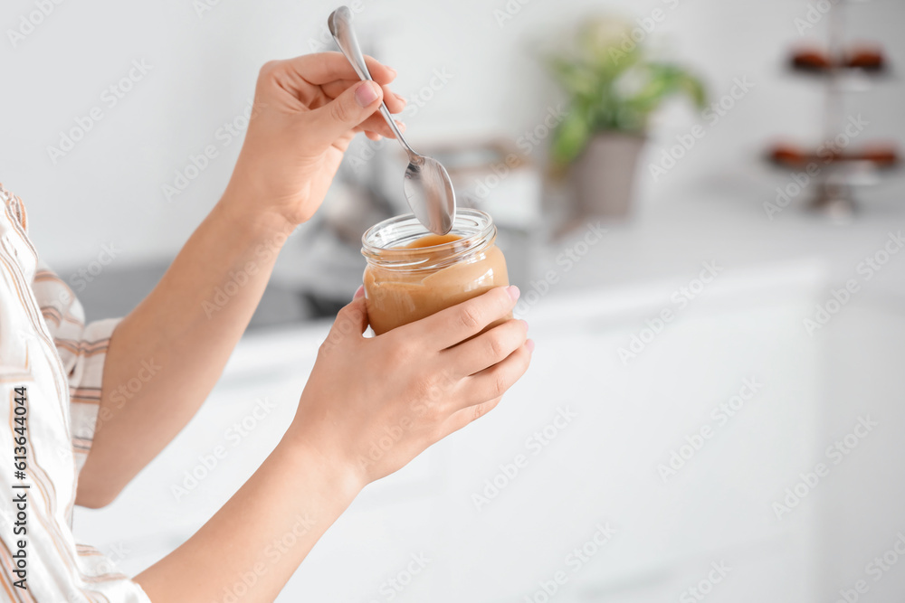 Young woman with spoon and jar of nut butter in kitchen, closeup