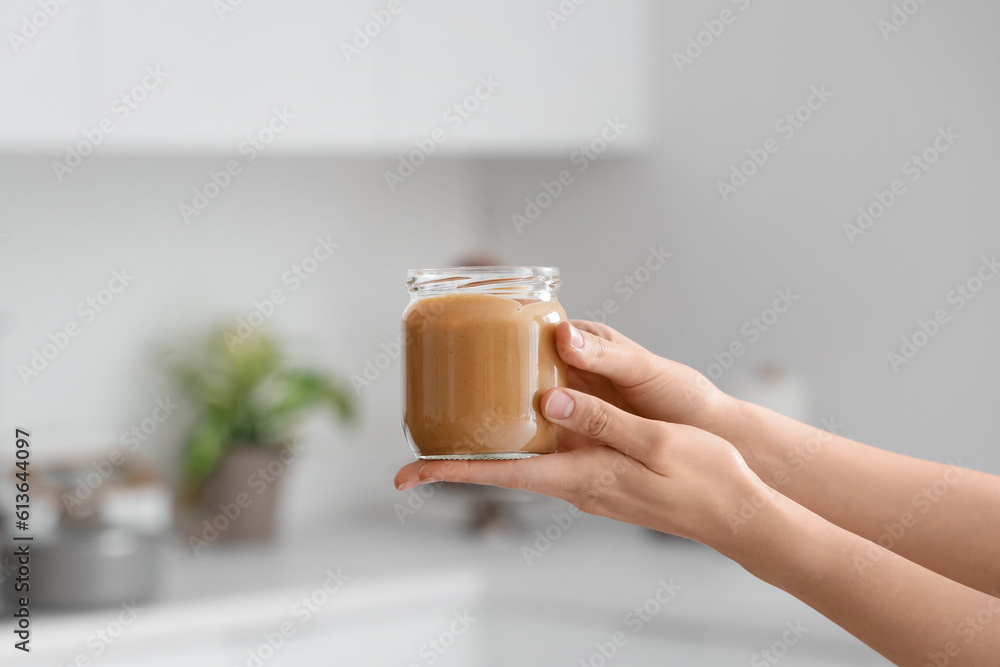 Young woman with jar of nut butter in kitchen, closeup